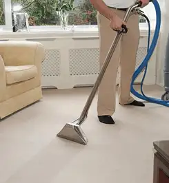Professional carpet cleaner using a hot-water extraction wand and hose machine in a living room in Yonkers, NY.