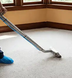 Steam carpet cleaning technician using a hot-water extraction wand on a residential carpet, wearing blue protective shoe covers Yonkers, NY.