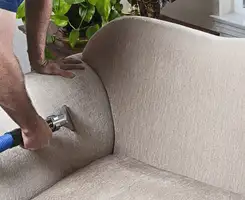 Professional upholstery cleaner deep-cleaning a fabric sofa with a handheld extraction tool and hose in Yonkers, NY.